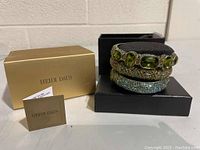 Photo showing three Heidi Daus bracelets stacked together on a black cushion, with original gold Heidi Daus box and folded card beside it.