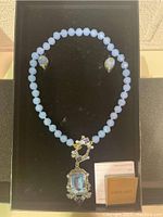 Full view of the necklace with light blue faceted beads and pendant, with matching earrings on a black background display