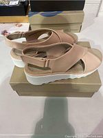 Side view of blush rose Clarks ladies sandals on their original box showing the thick white platform sole and crossover strap.