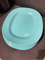 Stack of 10 turquoise square plates with rounded edges and a recessed center area for food.