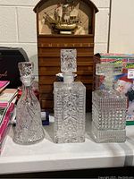 Three different styled glass decanters with stoppers on a table, detailed cut glass designs visible