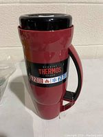 Photo of front view of new red Thermos travel mug with black handle and lid, showing branding and capacity info