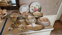 Wide view of assorted antique and vintage china on a countertop including plates, bowls, and serving dishes with floral patterns and gold accents.