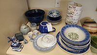 Overall view of assorted ceramic bowls, plates, and decorative items including blue and white patterns, floral motifs, and solid colors.