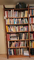 Wooden bookshelf containing six shelves of various books ranging in topics with mostly colorful spines visible