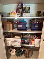 Wide view of closet shelving showing storage bins with ribbons, boxes of candles on bottom shelf, and wrapping paper in upright organization containers on top shelf.