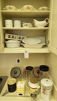 Kitchen counter displaying variety of canisters including black, floral decorated, and yellow-striped ceramic, plus metal kitchen utensil.