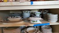 Wide view of multiple stacks of dinnerware including plates, bowls, and stands with raspberry and leaf pattern.
