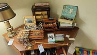 Wide group shot of all jewelry boxes, necklaces, bracelets, brooches, and miscellaneous items on a wooden table including a desk lamp.