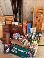 Full overview of assortment showing multiple wooden cribbage boards, boxed sets, card decks and peg bags