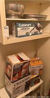 Shelf with Cuisinart Mandolin Slicer box, two Crock-Pot boxes, and metal bowls above them