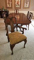 Dining set photo showing 6 chairs around a dining table, highlighting armchair in front with upholstered patterned seat and carved wood back.