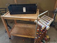 Wooden garden cart with wire planter box placed on top and croquet set on the side.