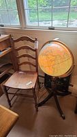 Wood ladder-back side chair beside the illuminated globe on stand near window