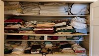 Three shelves filled with folded linens including blankets, placemats, various towels and napkins