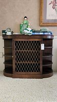 Full front view of the mahogany side cabinet showing the metal grille door, side curved shelves, and items on top.