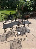 Four black metal patio chairs arranged on concrete patio outside in daylight, showing design and condition of each chair.