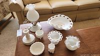 Milk glass lamp with hobnail shade, decorative bowl, candlestick holders, small covered dish, and compote dish all displayed on wood table.