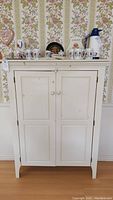 Front view of white pantry cupboard showing double doors, molding along the top, round door knobs, with some marks on front.