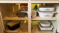 Wide view of shelves with multiple glass and ceramic baking dishes from Pyrex and CorningWare with lids mostly on top shelf.