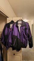 Two purple and black Colorado Rockies jackets hanging on hangers showing front views.