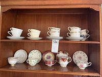 Two shelves of assorted tea cups and saucers showing various floral and patterned designs in white porcelain and porcelain with colorful prints and gold accents.