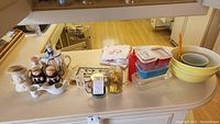 Overview of all items including Pyrex dishes, bowls, kitchen towels, teapot, figurines, and small jars on a countertop.
