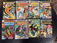 Eight comics laid out on black table: Marvel Tales, Human Torch issues, Power Man and Iron Fist issues, Black Panther, Sgt. Fury