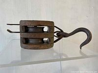 Side view of the antique wooden nautical pulley showing double metal sheaves and large metal hook.