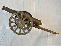 Side angle view of the brass cannon replica showing details of the barrel, wheels, and carriage.