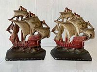 Front view of two cast iron galleon ship bookends, showing detailed sails and hull, painted beige and red with cross emblems on sails.