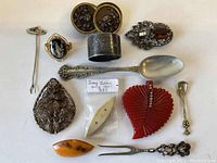Photo showing full lot layout including napkin ring, hair clips, silver spoon, bodkin in plastic bag, red carved ornament, and other small items.