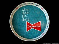 Photo showing the full flat front face of the round tray with blue textured background and red Budweiser bow-tie logo with text reading 'where there's life... there's Budweiser' and ringed rim with 'KING OF BEERS'.