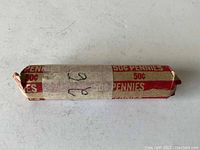 Photo of roll of pennies wrapped in red and white paper labeled '50¢ PENNIES' with handwritten '26'