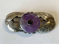 Front view of a sterling silver brooch with a central circular amethyst stone and leaf pattern on the sides.