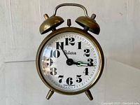 Front view of vintage Bulova twin bell alarm clock showing white dial with black numerals and brass metal casing.