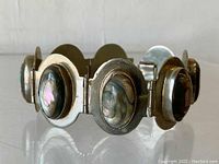 Side angled view showing sterling silver bracelet with large mother of pearl ovals and hinged links.