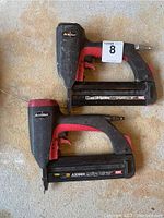 Photo of two black and red Accuset brad nailers placed side by side on a concrete floor, showing overall shape and wear.