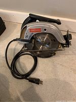 View of full Craftsman circular saw with cord coiled beside it on floor.