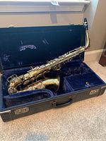Evette alto saxophone resting inside its open hard case with blue velvet lining. Shows overall view including saxophone body, keys, and interior compartments.
