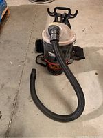 Front view of Shoulder Vac Pro Commercial Backpack Vacuum with attached flexible hose and harness for carrying.