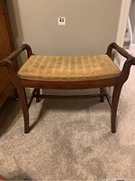 Front view of vintage wooden bench with side handles and upholstered seat showing wear.