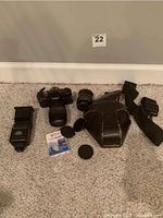 Photo of Minolta X-700 camera, extra lens, flash, camera strap and leather case with lens caps and cleaning cloth on beige carpet.
