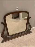 Front view of vintage dresser mirror showing rectangular mirror with rounded top corners set in dark wooden frame with curved wooden supports on sides