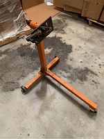 Orange engine stand with a horizontal base, three caster wheels, and a vertical post supporting a black rotating engine mount.