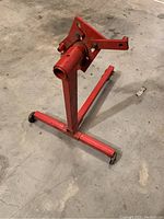 Red engine stand on a concrete floor showing the vertical support and base with wheels.