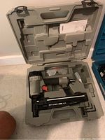 Porter Cable finish nailer, model FN250A, inside its hard plastic carrying case with safety glasses and lubricant bottle.
