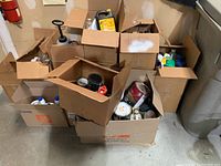 Boxes filled with various household chemicals, paints, and automotive fluids on a concrete floor