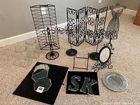 Full view of jewelry stands and bases spread on floor, showing all items in lot including black metal stands, mirror bases, glass jars, and acrylic letters.