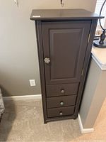 Front view of the tall brown lingerie chest showing three drawers with decorative knobs and one door with decorative knob.